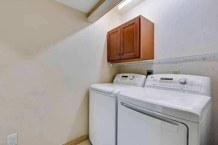 Laundry area with a textured wall, cabinet space, and washer and clothes dryer