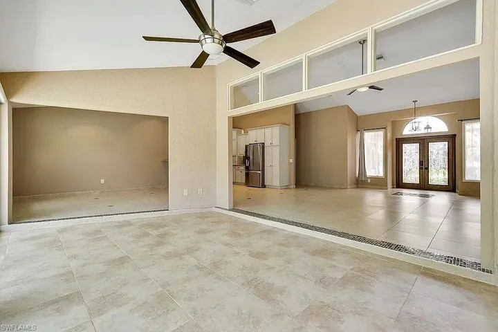 Unfurnished living room featuring baseboards, tile patterned floors, french doors, a ceiling fan, and high vaulted ceiling