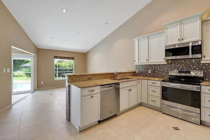 Kitchen featuring a sink, a peninsula, stainless steel appliances, backsplash, and stone countertops
