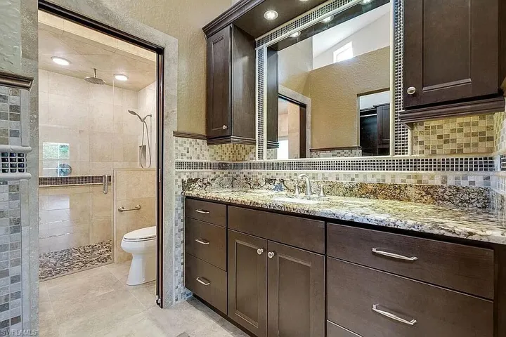 Bathroom featuring vanity, tile patterned flooring, toilet, a shower stall, and decorative backsplash