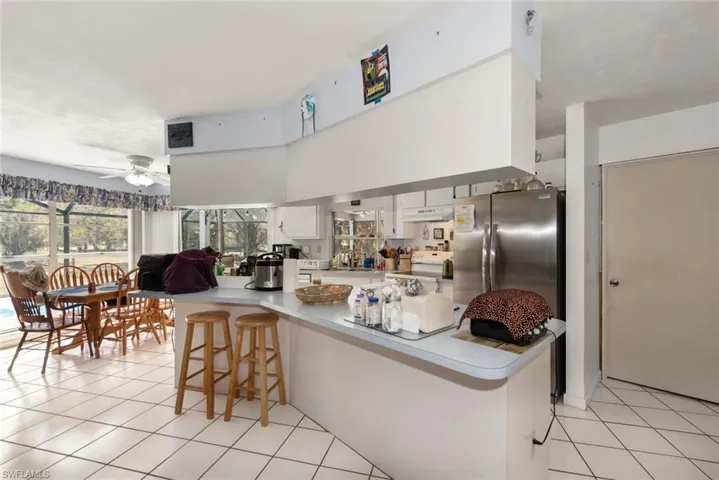 Kitchen featuring a breakfast bar, ceiling fan, light countertops, light tile patterned floors, and white cabinetry