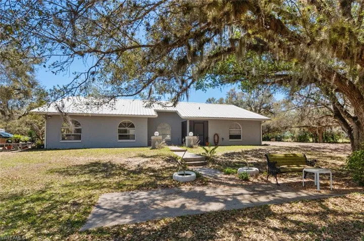 Back of property featuring a metal roof, stucco siding, a lawn, and a patio