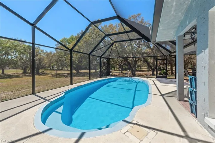 Outdoor pool featuring a sunroom, a patio area, glass enclosure, and a lawn
