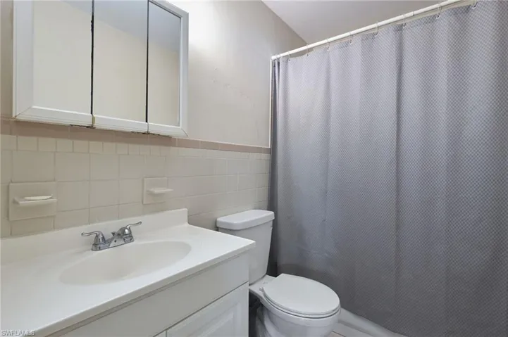 Bathroom featuring tasteful backsplash, tile walls, vanity, and toilet