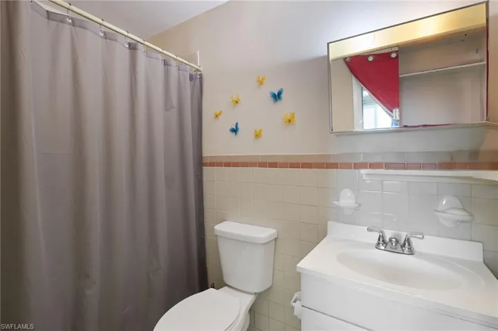 Bathroom featuring backsplash, tile walls, vanity, and toilet