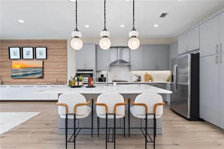 Kitchen featuring stainless steel refrigerator with ice dispenser, gray cabinetry, wall chimney exhaust hood, and an island with sink