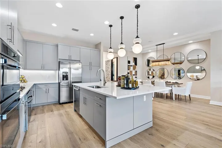 Kitchen featuring stainless steel appliances, sink, pendant lighting, gray cabinets, and an island with sink