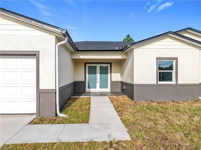 Property entrance featuring stucco siding, french doors, a garage, and a lawn
