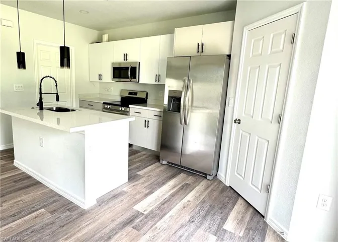 Kitchen featuring appliances with stainless steel finishes, white cabinetry, a center island with sink, and hanging light fixtures