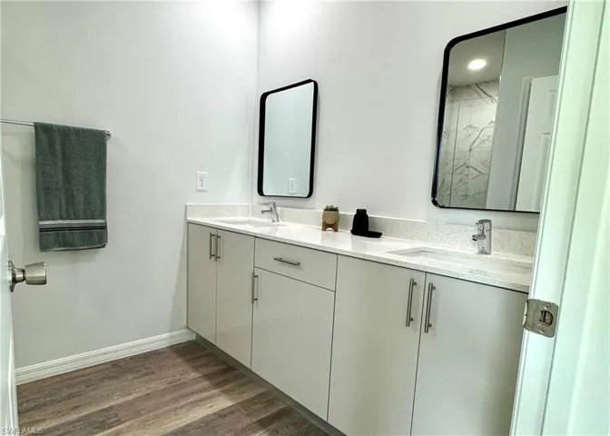 Bathroom with double vanity and dark wood-type flooring