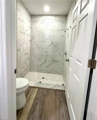 Full bathroom with dark wood finished floors and a marble finish shower