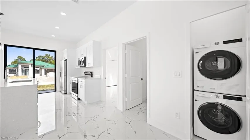 Laundry area with stacked washer / dryer, recessed lighting, and light marble finish flooring