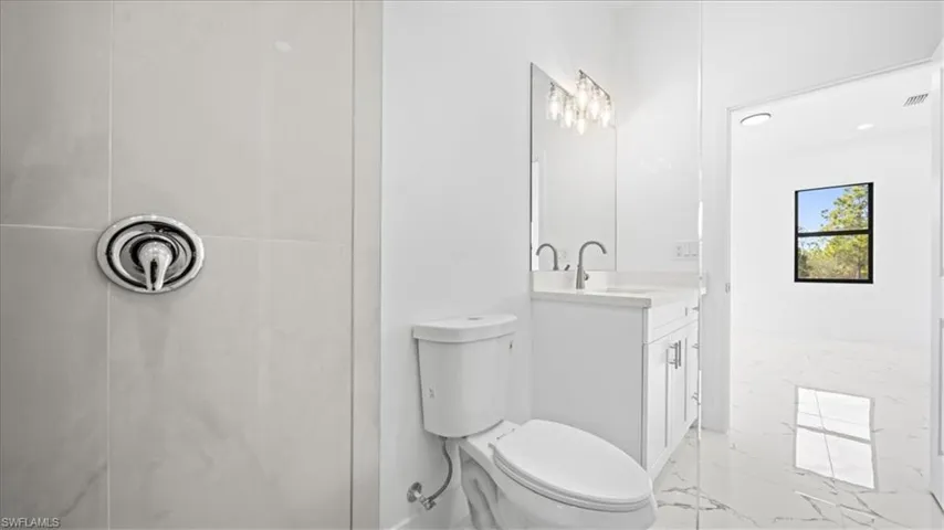 Bathroom with tiled shower, vanity, and light marble finish flooring