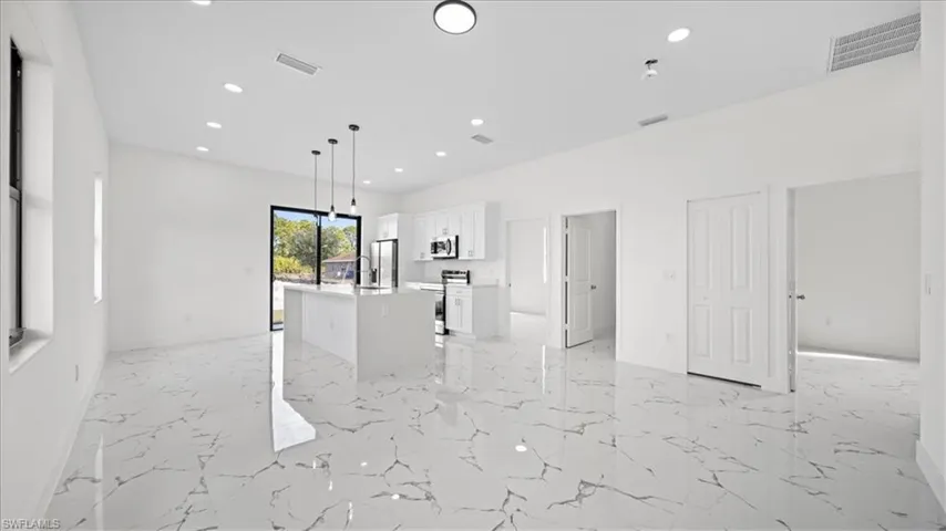 Kitchen featuring pendant lighting, open floor plan, white cabinets, an island with sink, and stainless steel appliances