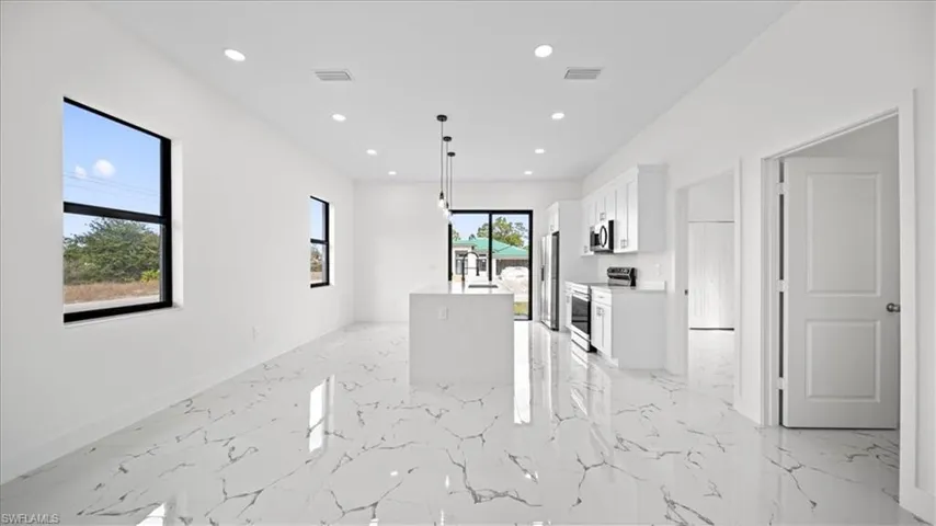 Kitchen featuring pendant lighting, stainless steel appliances, white cabinetry, an island with sink, and light marble finish flooring