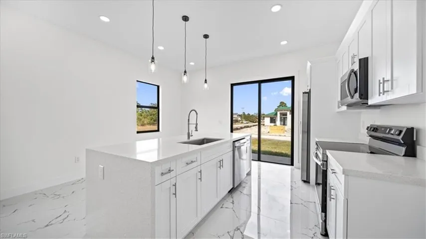 Kitchen with stainless steel appliances, white cabinets, light marble finish floors, light stone countertops, and pendant lighting