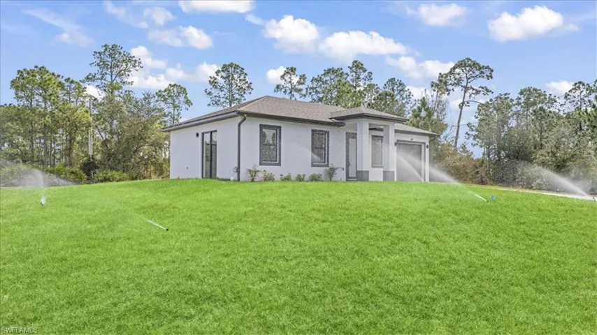 Back of house featuring a yard, stucco siding, an attached garage, and view of wooded area