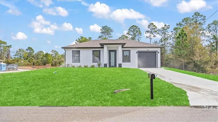 Prairie-style home featuring concrete driveway, a garage, stucco siding, a front lawn, and roof with shingles