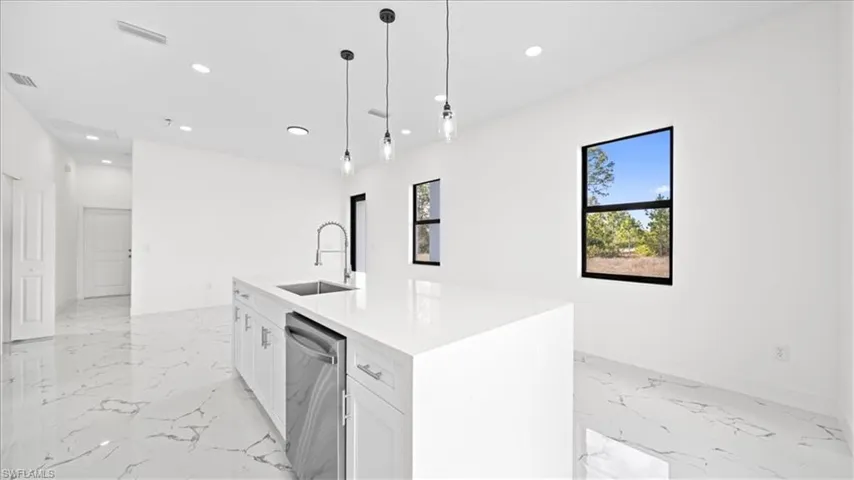 Kitchen featuring white cabinets, decorative light fixtures, light stone countertops, stainless steel dishwasher, and a kitchen island with sink