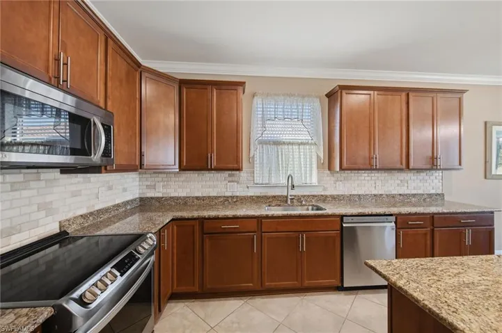 Kitchen with stainless steel appliances, wood finish cabinetry, light stone countertops, and crown molding