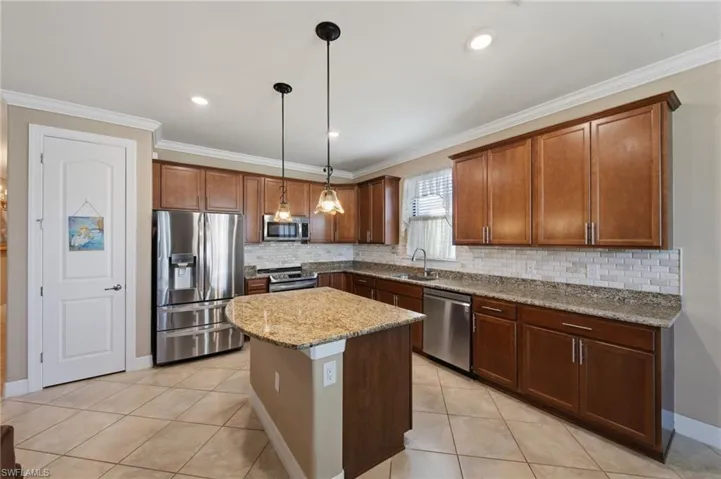 Kitchen with stainless steel appliances, pendant lighting, light stone countertops, a kitchen island, and ornamental molding