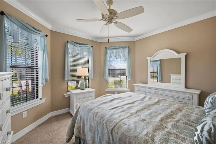 Bedroom with light colored carpet, ornamental molding, and a ceiling fan