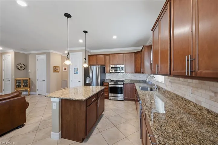 Kitchen featuring backsplash, light tile patterned floors, stainless steel appliances, crown molding, and light stone counters