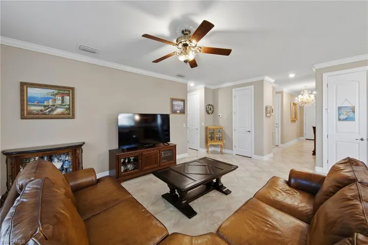 Living area with ornamental molding, a chandelier, ceiling fan, and light tile patterned floors