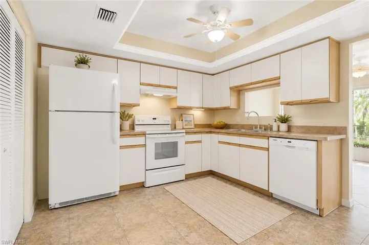 Kitchen featuring white appliances, upper and lower cabinetry, a built-in sink, and tile flooring