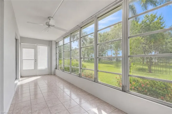 Enclosed sunroom featuring a full wall of windows, tile flooring, a ceiling fan, and access to the exterior