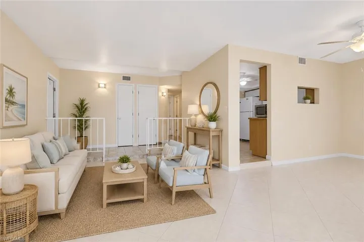 Open-concept living area featuring light-colored tile flooring, neutral wall tones, a ceiling fan, and a pass-through window to the kitchen