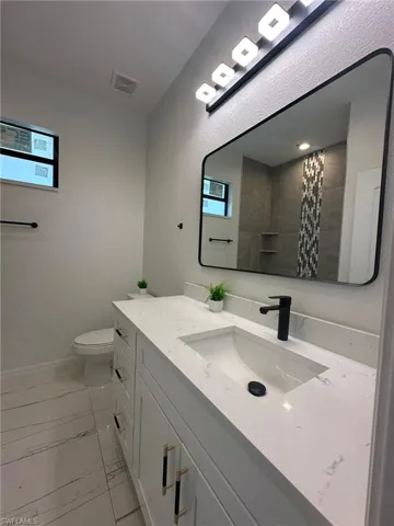 Bathroom with tile patterned flooring, a healthy amount of sunlight, toilet, and vanity