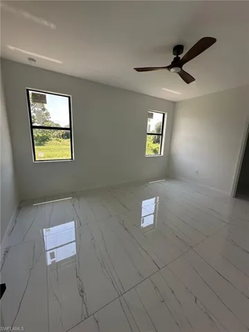 Empty room featuring light tile patterned flooring, a wealth of natural light, and ceiling fan