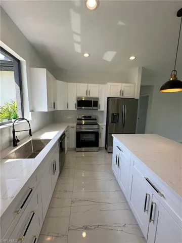 Kitchen with appliances with stainless steel finishes, light stone counters, pendant lighting, white cabinets, and light tile patterned flooring