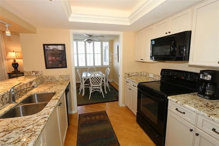 Kitchen with light hardwood / wood-style flooring, a raised ceiling, white cabinetry, black appliances, and sink