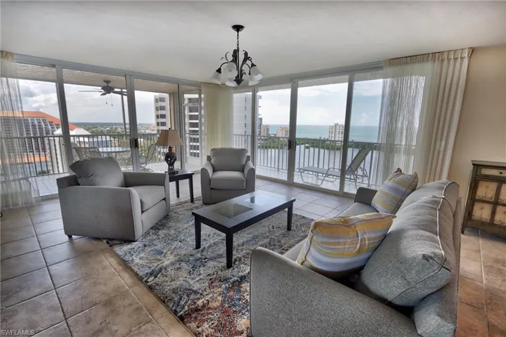 Tiled living room featuring a wall of windows, a water view, and ceiling fan with notable chandelier