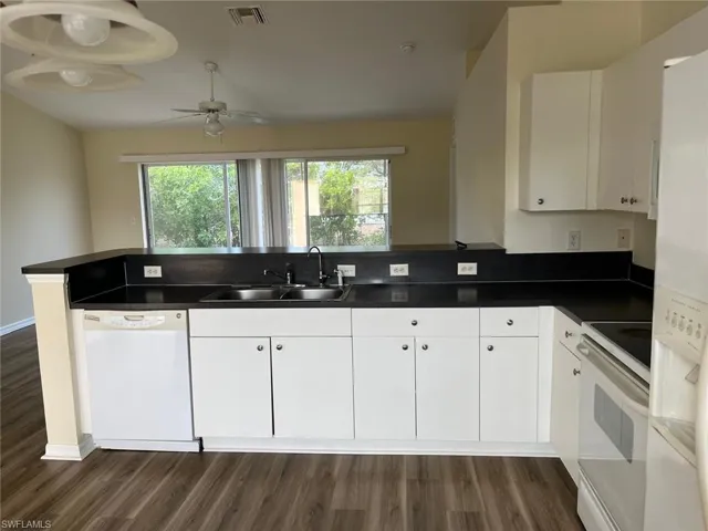 Kitchen with white appliances, dark countertops, white cabinets, and dark wood finished floors