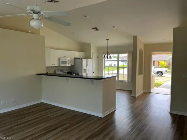 Kitchen featuring dark countertops, a breakfast bar area, white appliances, dark wood finished floors, and ceiling fan