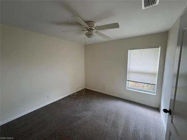 Empty room featuring dark carpet and ceiling fan
