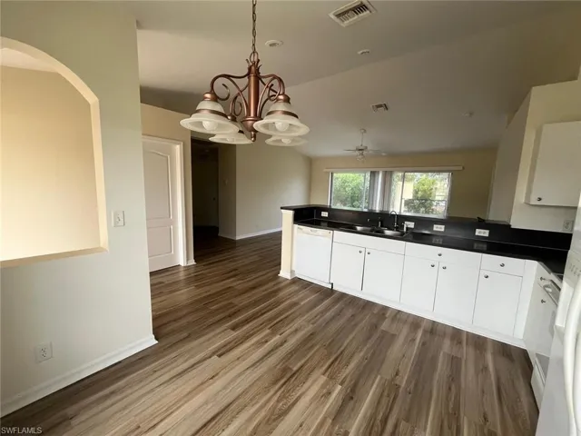 Kitchen with dark countertops, white cabinets, vaulted ceiling, white dishwasher, and hanging lights