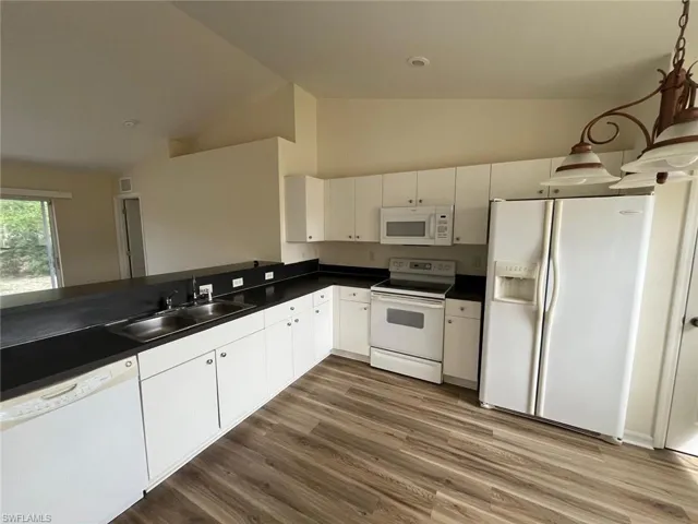 Kitchen featuring dark countertops, white appliances, white cabinets, dark wood-type flooring, and decorative light fixtures