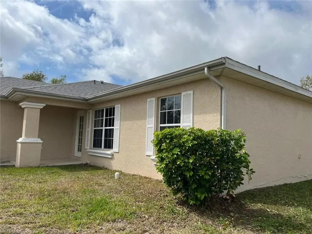 View of property exterior featuring stucco siding, a yard, and roof with shingles