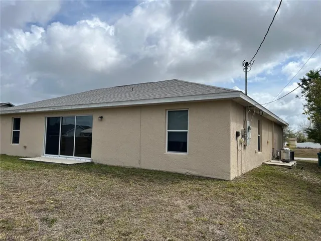 Back of property with stucco siding, a yard, and roof with shingles