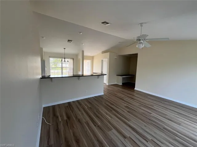 Unfurnished living room with dark wood-style floors, vaulted ceiling, ceiling fan, and a chandelier