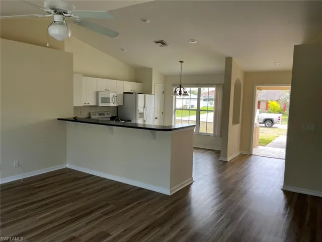 Kitchen with a kitchen bar, dark countertops, white appliances, a peninsula, and dark wood finished floors
