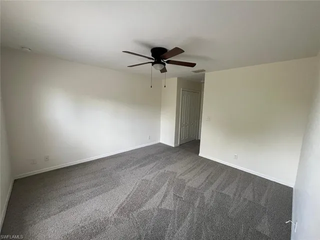 Unfurnished room featuring dark carpet and ceiling fan
