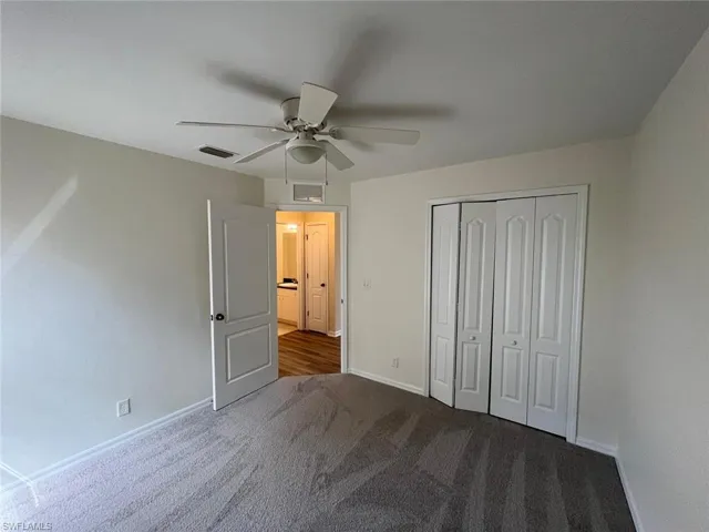 Unfurnished bedroom with dark colored carpet, a ceiling fan, and a closet