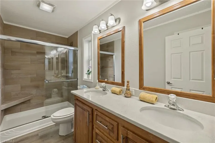 Bathroom with hardwood / wood-style floors, a shower with shower door, vanity, crown molding, and toilet