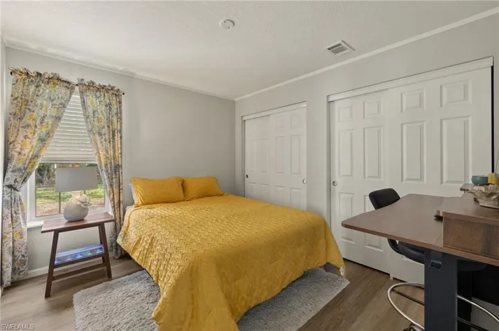 Bedroom featuring a textured ceiling, ornamental molding, hardwood / wood-style floors, and multiple closets