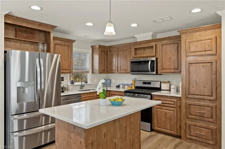 Kitchen with light wood-type flooring, stainless steel appliances, decorative light fixtures, a center island, and sink